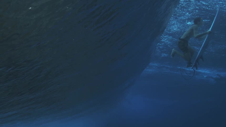 Surfer underwater pushing the board beneath a blue wave