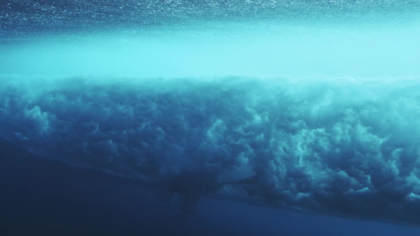 Surfboard moves over a breaking wave as the wave fills the water with bubbles