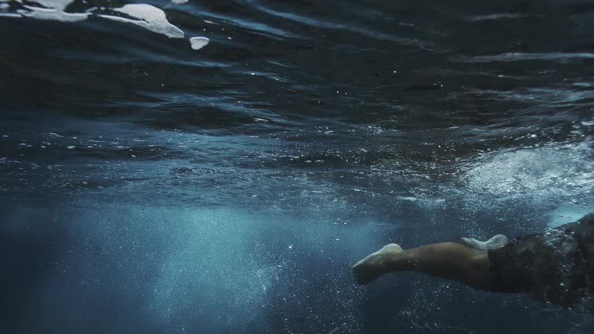 Person swimming beneath the ocean surface in deep waters