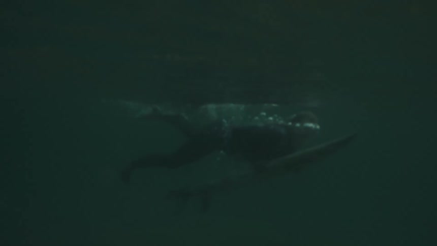 Surfer submerged with the board moving beneath the dark ocean surface