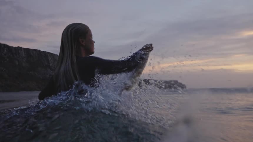 Person paddling on a surfboard in the sea at sunset