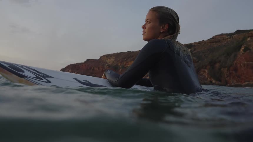 Surfer watching the sea while resting on the board near the rocks