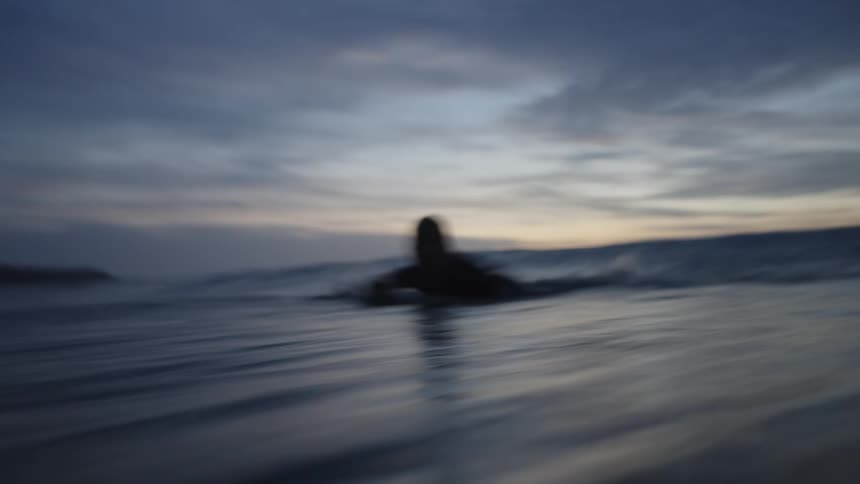Surfer floating on the board at sunset in the calm sea