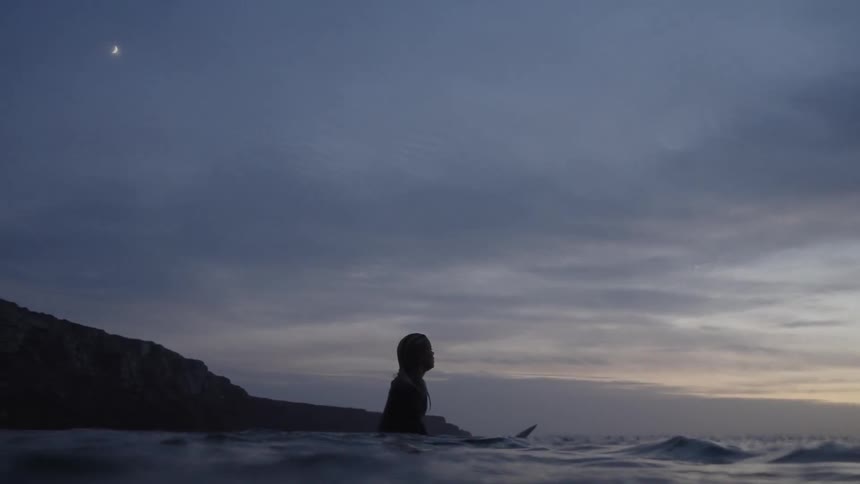 Woman with surfboard watching the horizon in the sea at dusk