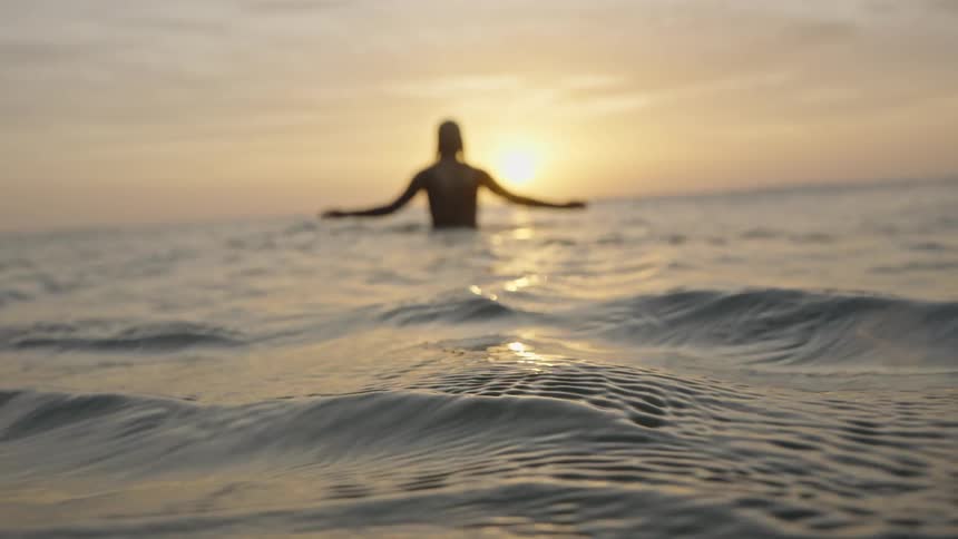 Surfer remains in the water watching the sunset over the ocean horizon