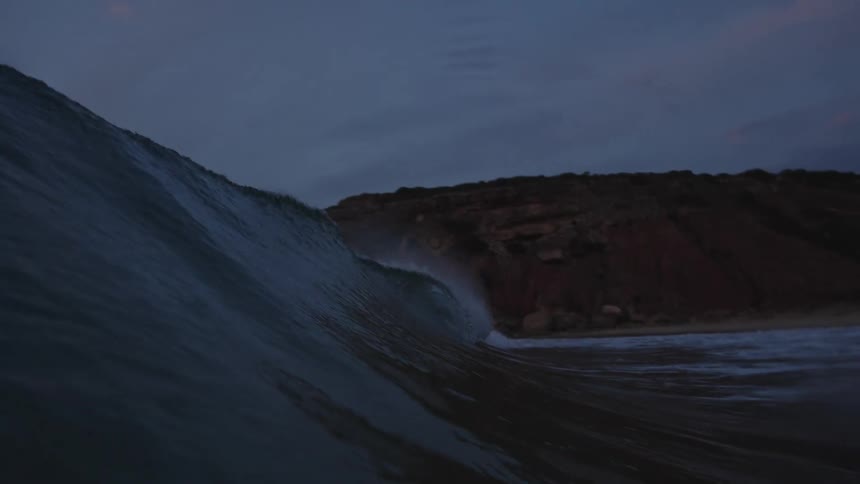 Wave forms near the rocky shore under a darkening evening sky
