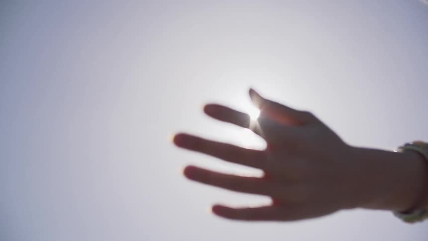 A woman's hand and arm extended towards the sky and lowering as the sun glares in the background