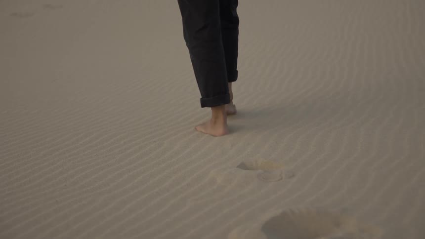 A man wearing pants is walking barefoot on the beach