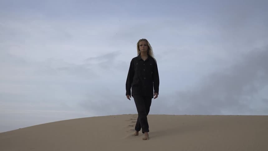 A female wearing black pajamas is walking on a sand hill in a desert