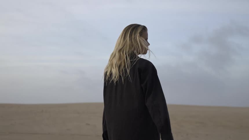 Woman with a serious expression standing in the desert under a cloudy sky