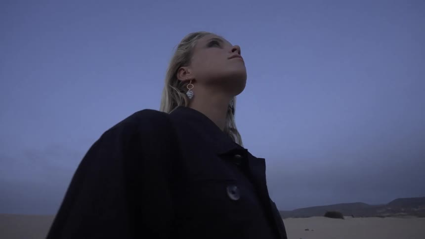 The woman is looking up at the sky on the beach