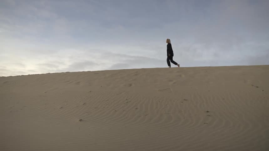A woman walks barefoot across desert sand at midday