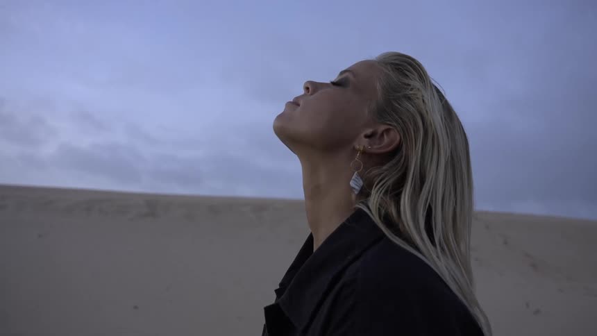 Woman with closed eyes lifts her face to the wind on the dunes at dusk
