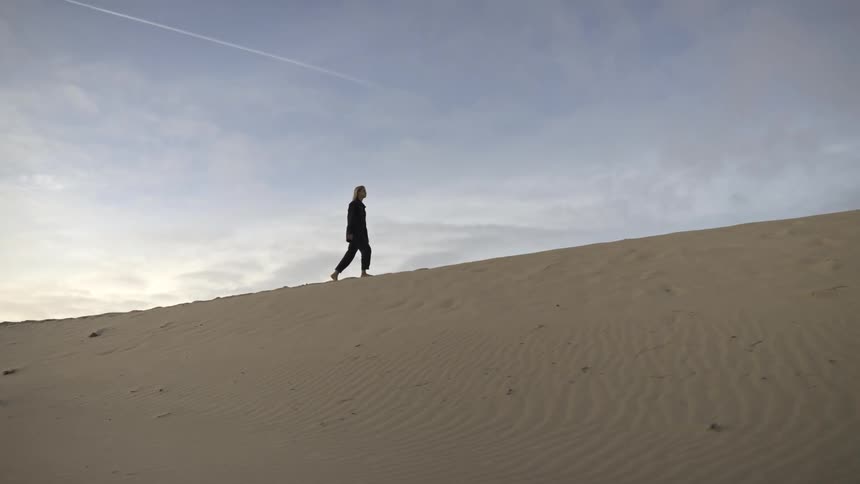 The woman hikes up the sand dune