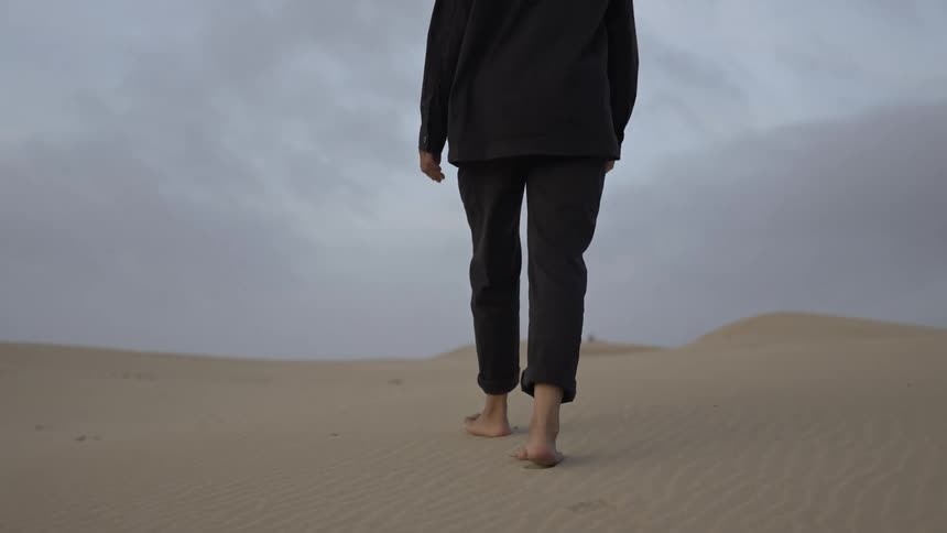 Person walking barefoot across the dunes under a cloudy sky