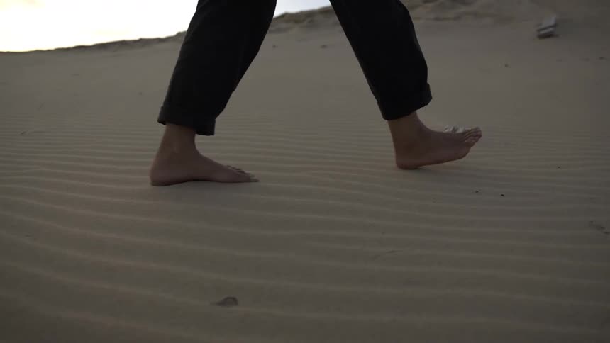 Woman walking barefoot on sand dunes at sunset