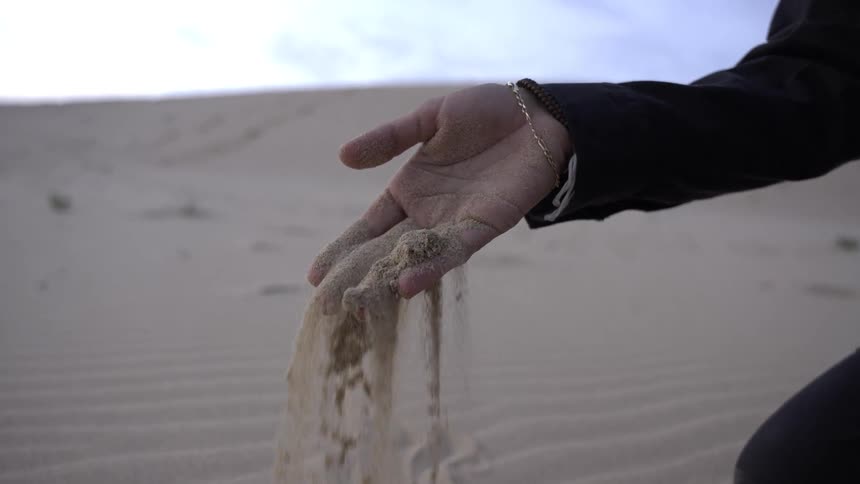 Hand lets sand slowly fall amid desert dunes