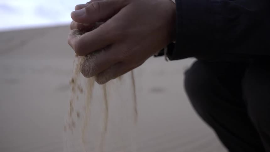 Hands clasp sand and then open allowing sand to stream between fingers back to the desert floor