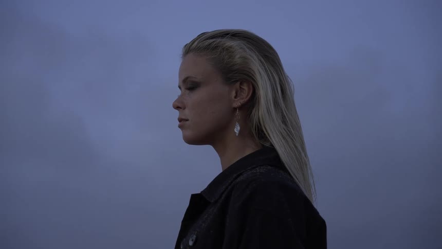 Woman gazes at the horizon at dusk with a contemplative expression under a bluishgray sky