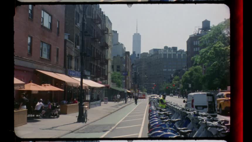 A city street view on a sunny day with cars driving along the road casting crisp shadows beneath the bright sky