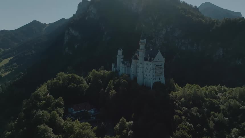 Aerial view of a european castle on a forested hill amid steep mountains