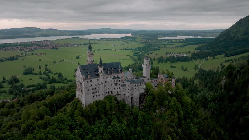 Castle stands on a forested mountain in the rural countryside near a town on an overcast day