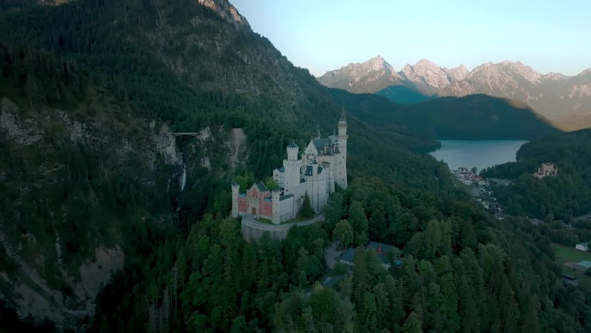 An aerial view showcases neuschwanstein castle nestled amongst lush forests near a lake and mountains
