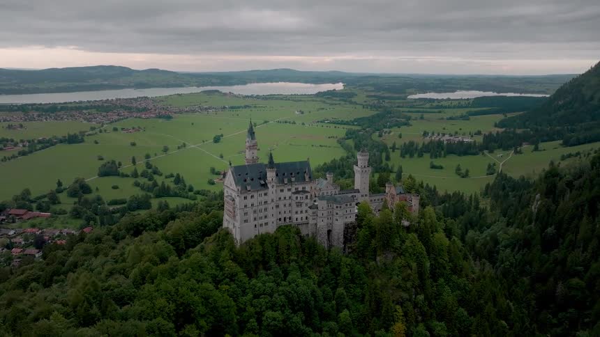 Castle stands on a forested mountain near a town in the rural countryside on an overcast day