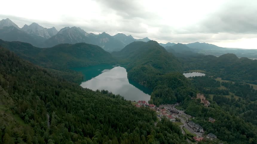 Aerial view of forested mountains with lakes and village under cloudy skies