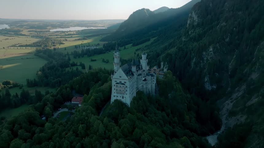 Castle stands on a forested hill in the shadow of the mountains in the rural countryside