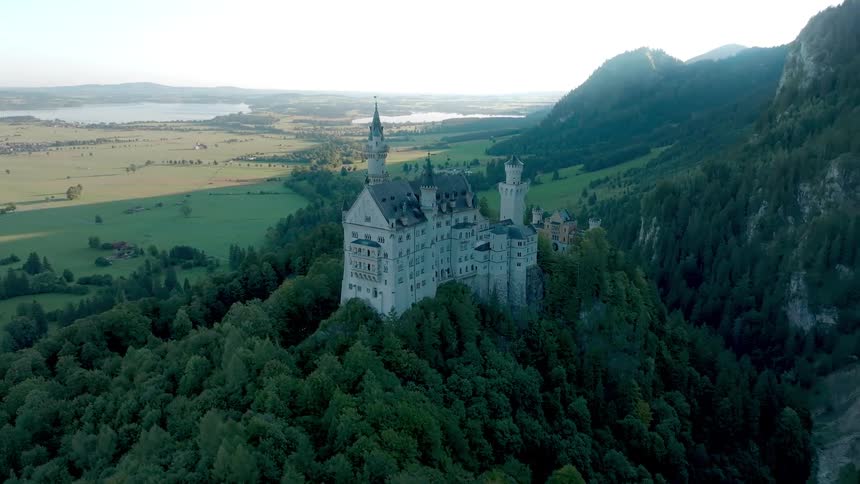 Aerial view of neuschwanstein castle on a forested hill with a distant mountains