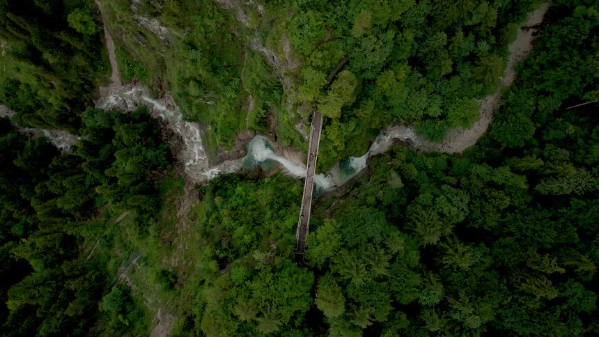 Aerial view of a wooden footbridge over rapids in a forested gorge