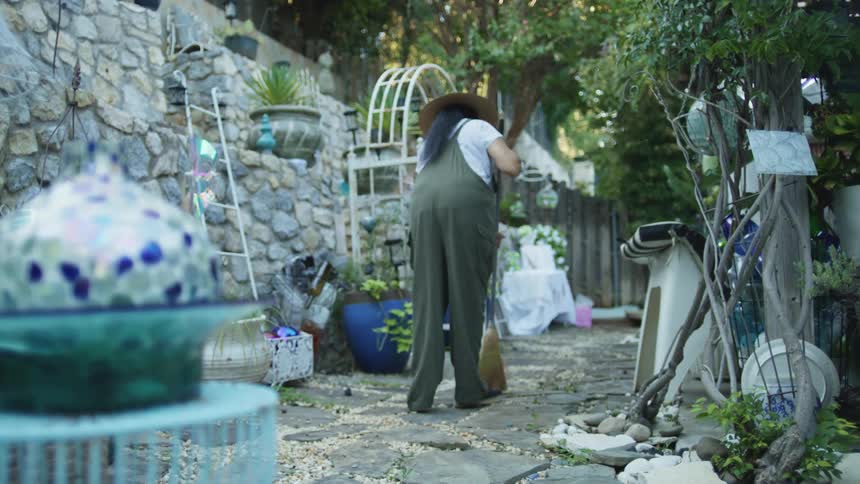 A woman sweeping a stone patio in a cluttered outdoor garden area