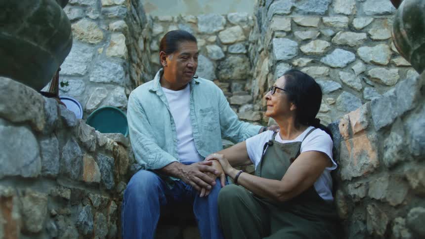 An affectionate older couple shares a tender moment talking and holding hands while sitting together on rustic stone steps