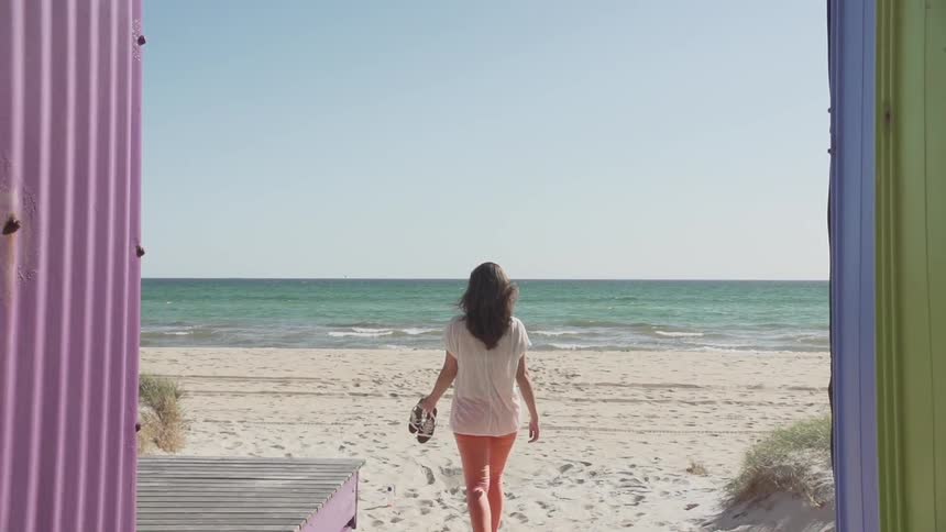 Woman carrying sandals walking onto the sand