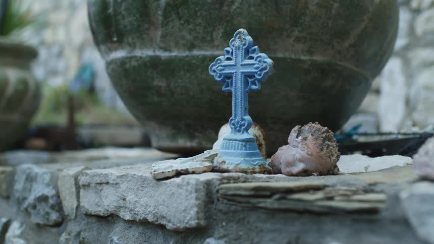 Small cross and the head broken off a statue lies on a stone shelf near a large stone pot during the daytime