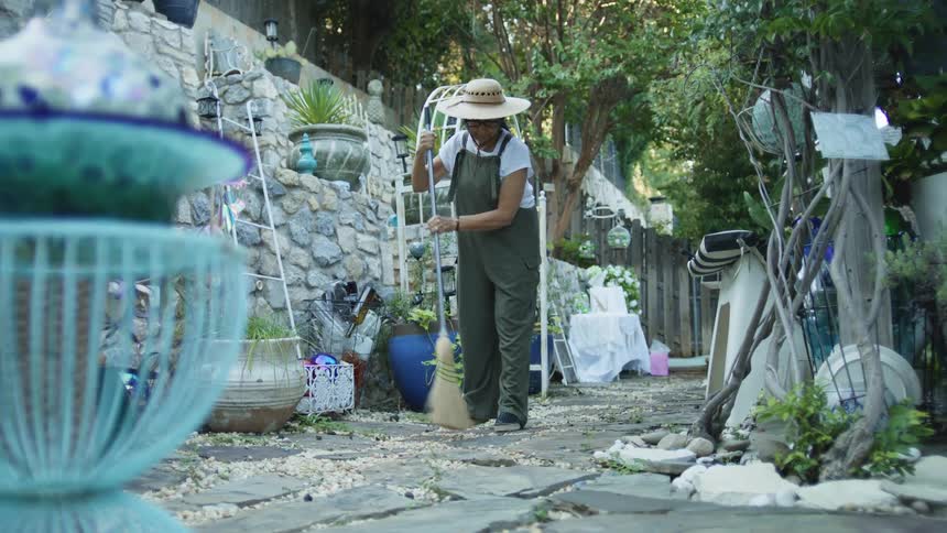 A middleaged gardener sweeps the backyard of a building at midday