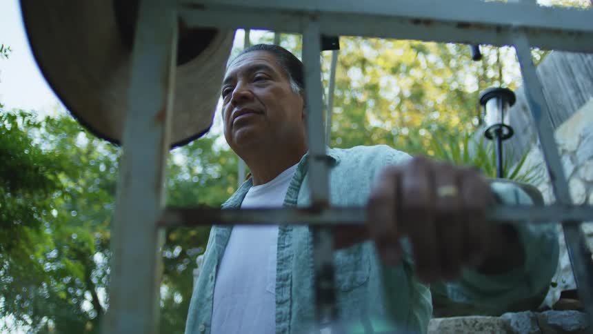 Man leaning on a metal gate with his hand resting and a hat hanging