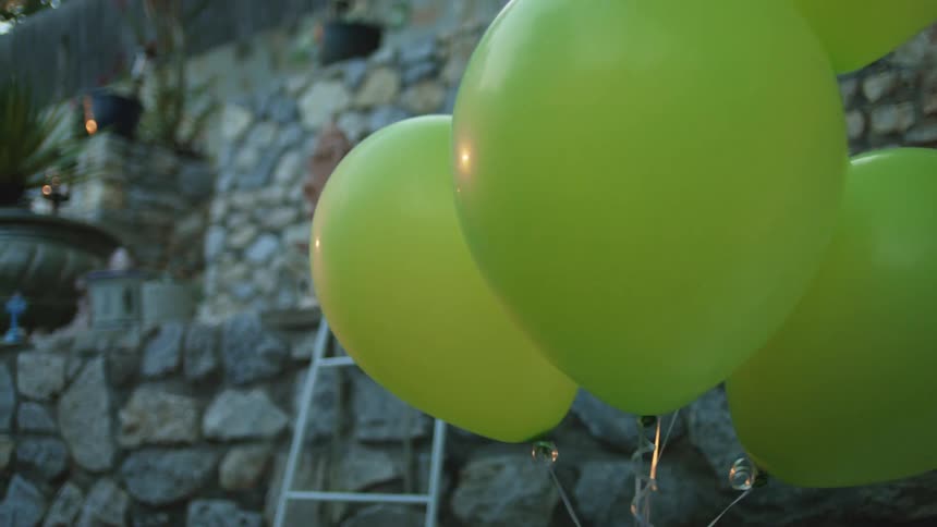 Yellow balloons float outdoors near a stone wall after dusk
