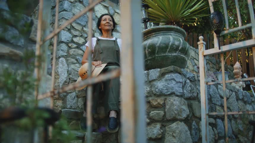 Woman sitting on stone steps holding a hat and looking upward