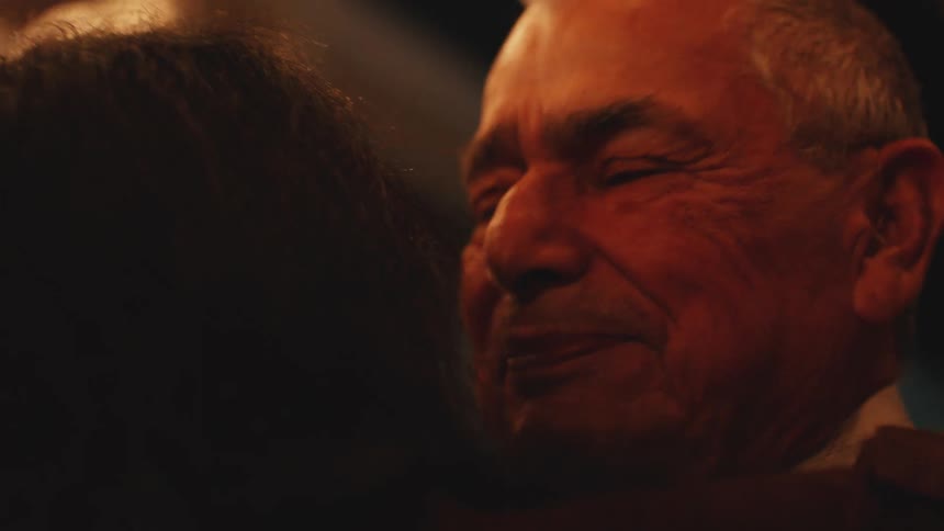 In a warm intimate close up an elderly man with a loving expression gently pulls back from a hug