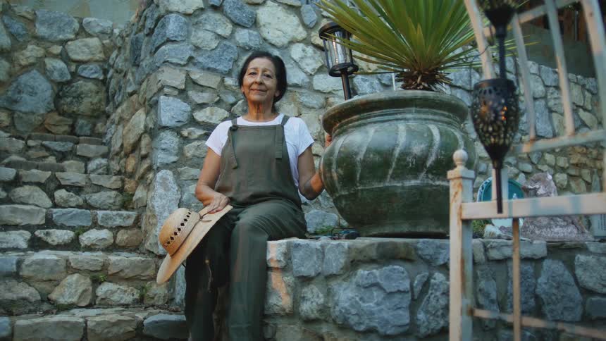 Woman sitting on a stone wall puts a hand on a potted plant