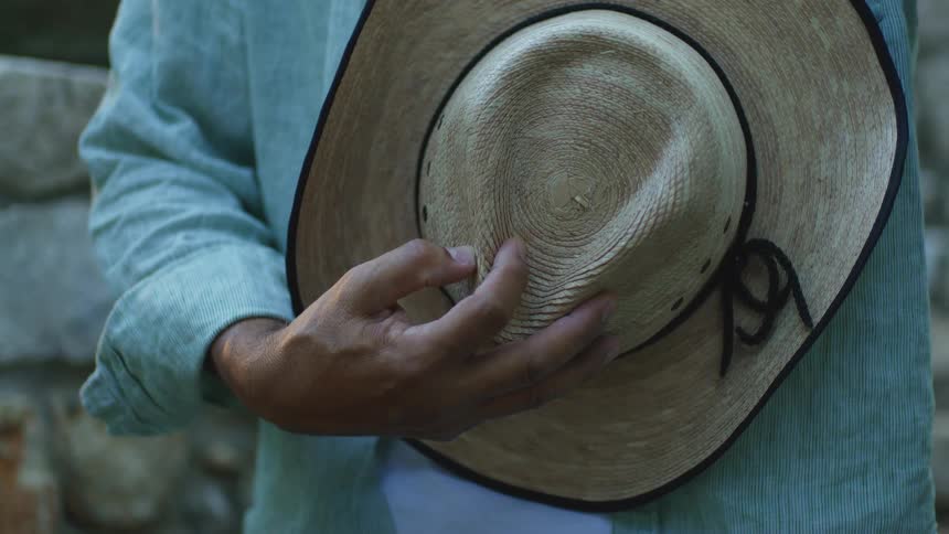 A person in a light blue shirt holds a woven straw hat by its crown