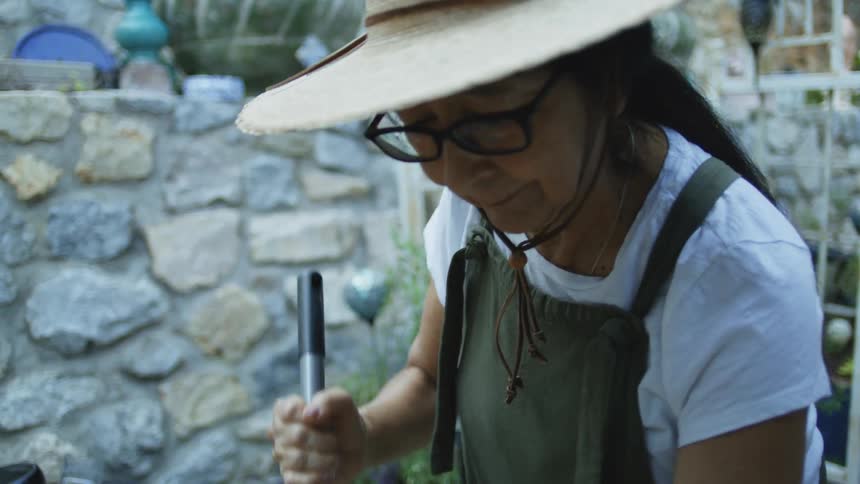 Woman wearing a straw hat works in the garden holding a tool