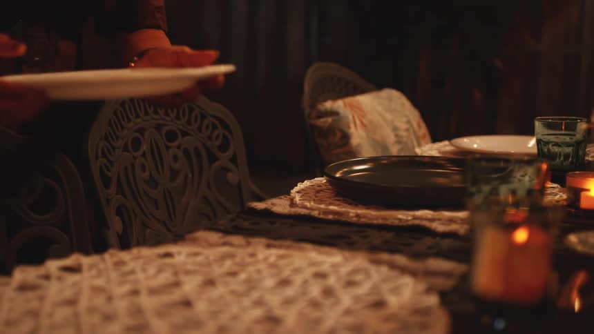 A woman sets a dinner table carefully placing plates down as she prepares for the evening meal