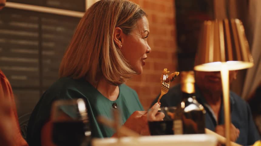 Smiling woman enjoying food and conversation with friends at a dinner table