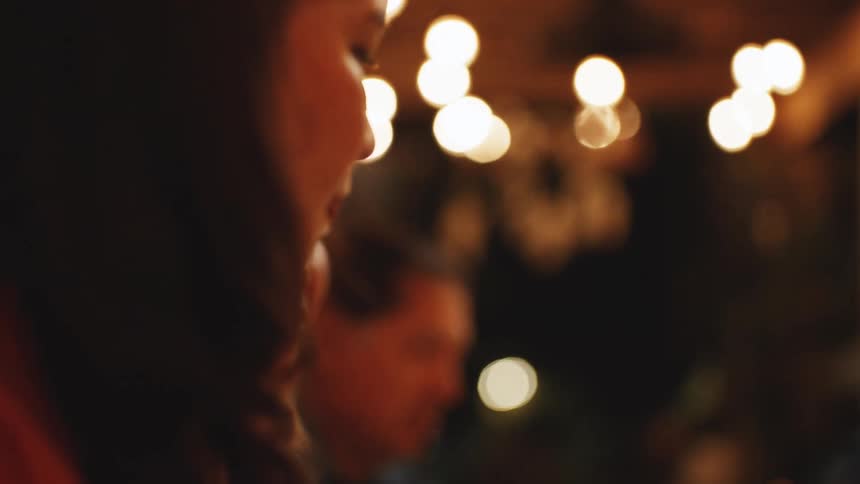 Hispanic woman at a restaurant table surrounded by a small group of people serving food on a tray indoors during night time