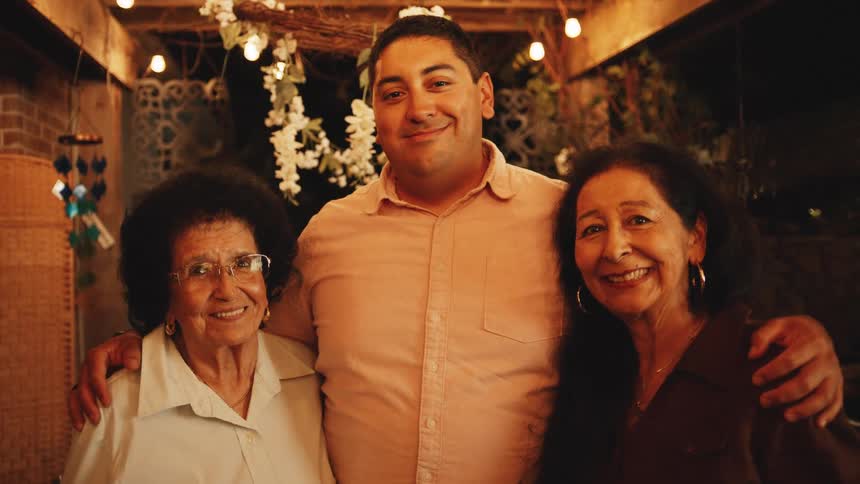 Three people smiling side by side in a setting decorated with lights and flowers