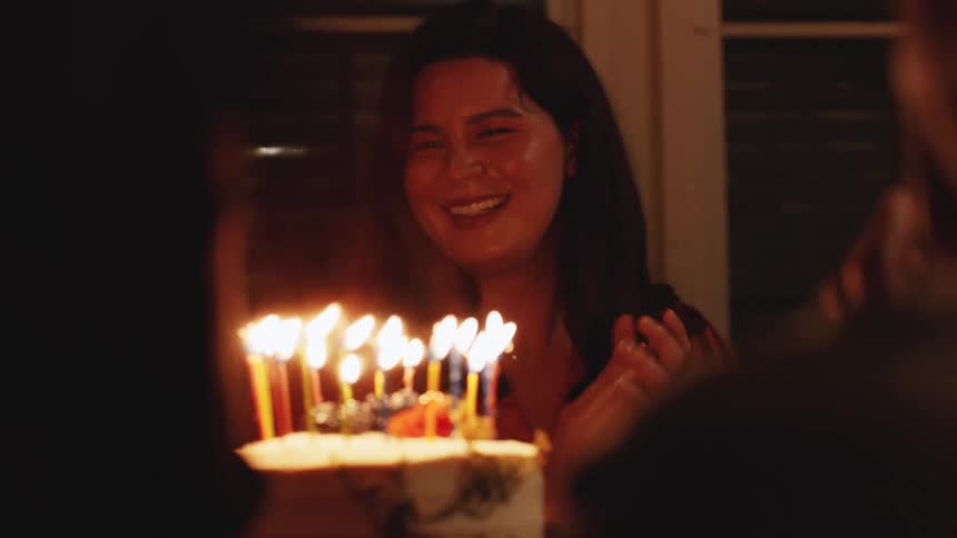 A group of people celebrate a birthday together in a dimly lit room