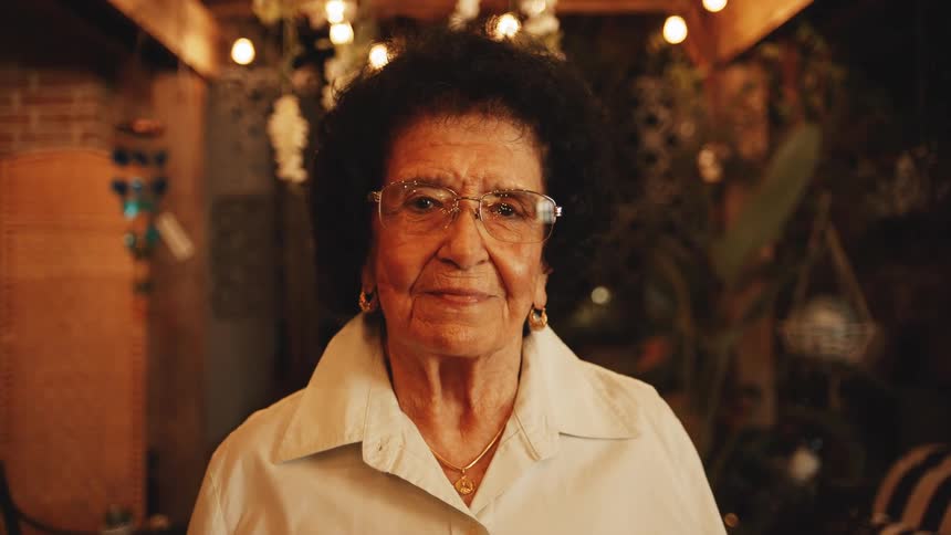 A smiling older woman looks into camera with blurred lights behind